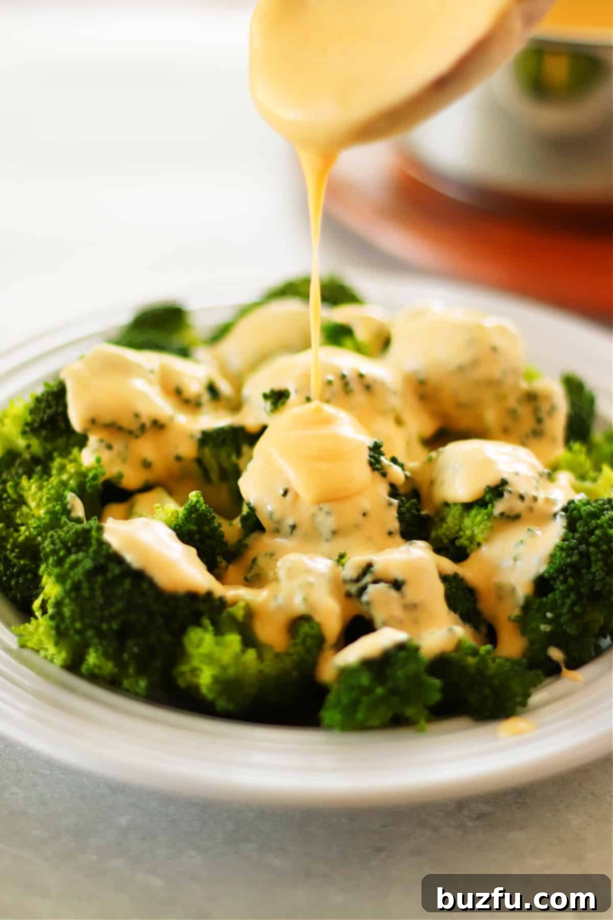 Best Creamy Cheese Sauce for Vegetables and More Cheddar cheese sauce drizzled generously over perfectly cooked steamed broccoli florets in a white bowl, ready to be enjoyed.