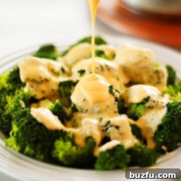 Velvety Cheese Sauce for Broccoli and More 3 Cheddar cheese sauce drizzled over cooked broccoli in a bowl, highlighting its creamy texture and rich color.