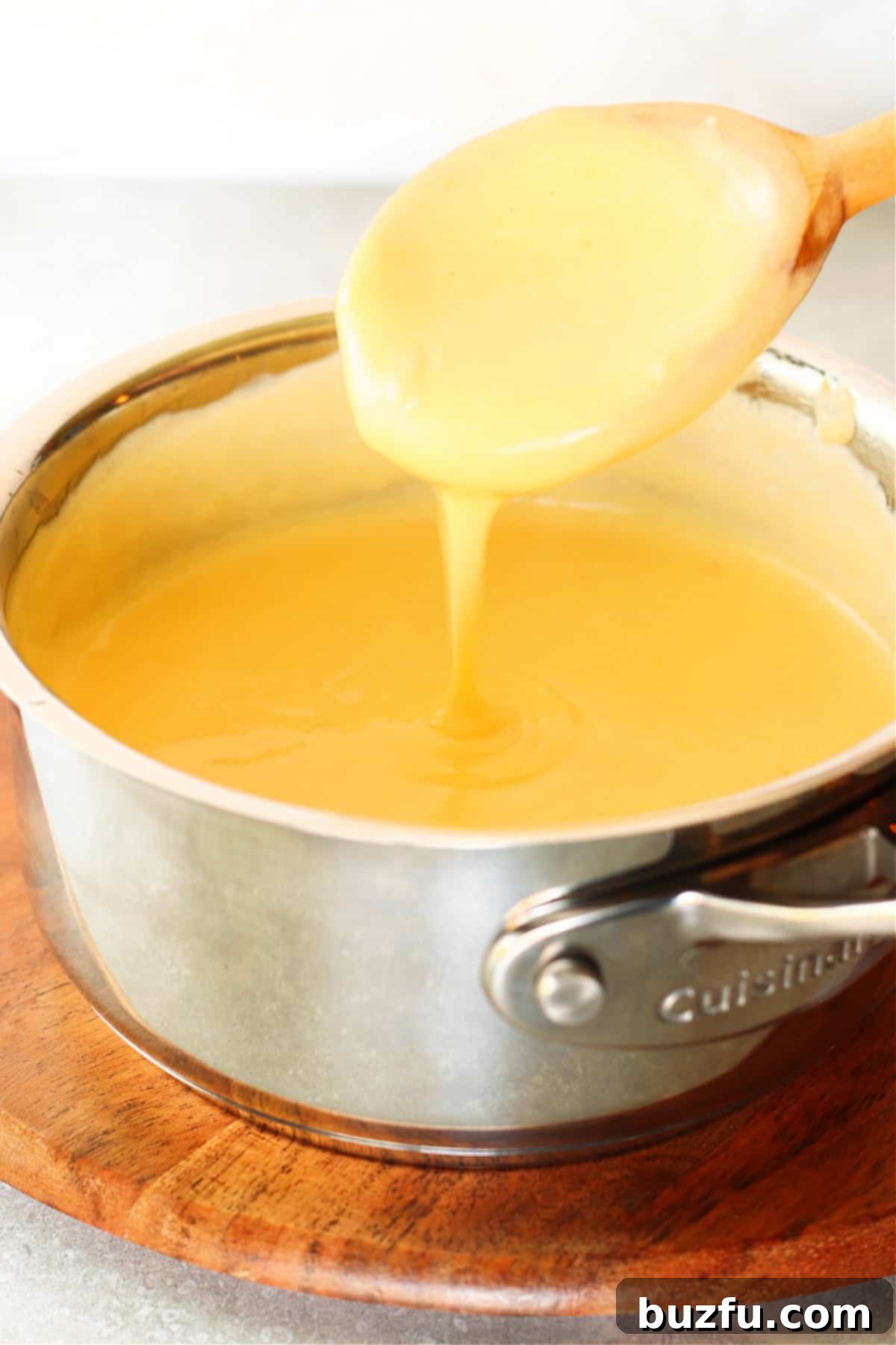 Versatile and Easy Homemade Cheese Sauce Close-up shot of rich, golden cheese sauce being drizzled from a wooden spoon, showcasing its perfect creamy consistency, held over the saucepan.