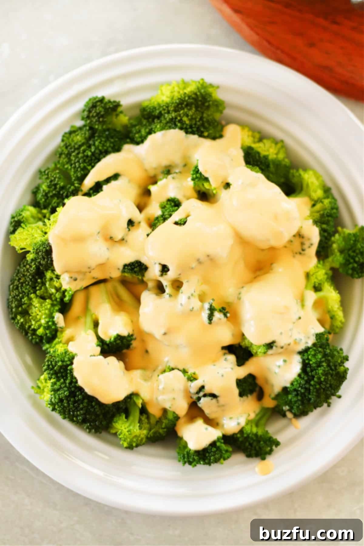 Perfect Cheese Sauce for Broccoli A close-up shot of fluffy steamed broccoli florets elegantly arranged on a white plate, generously coated with a rich, golden homemade cheese sauce, highlighting its appetizing appeal.