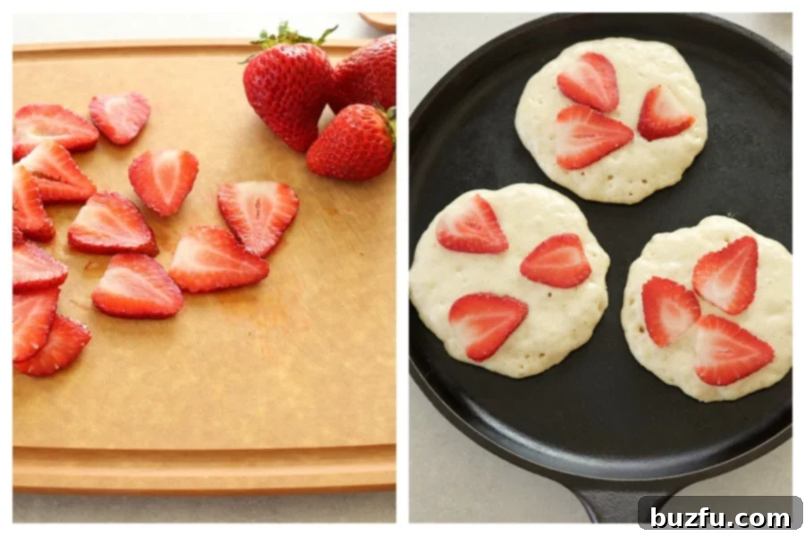 Thinly sliced strawberries are placed on top of pancake batter cooking on a griddle. Other sliced strawberries are visible on a cutting board.