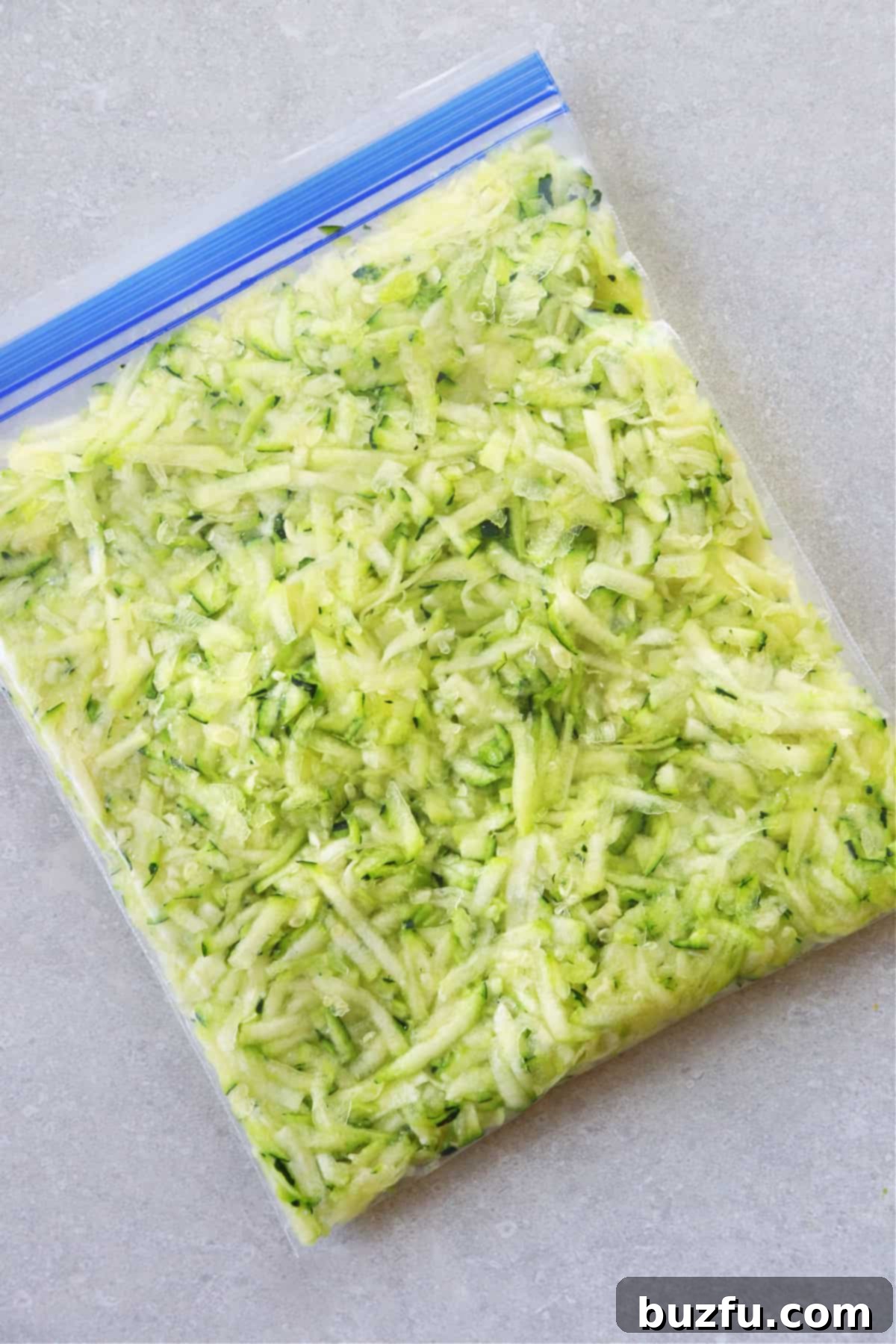 Freshly shredded zucchini in a clear freezer bag, ready for storage.