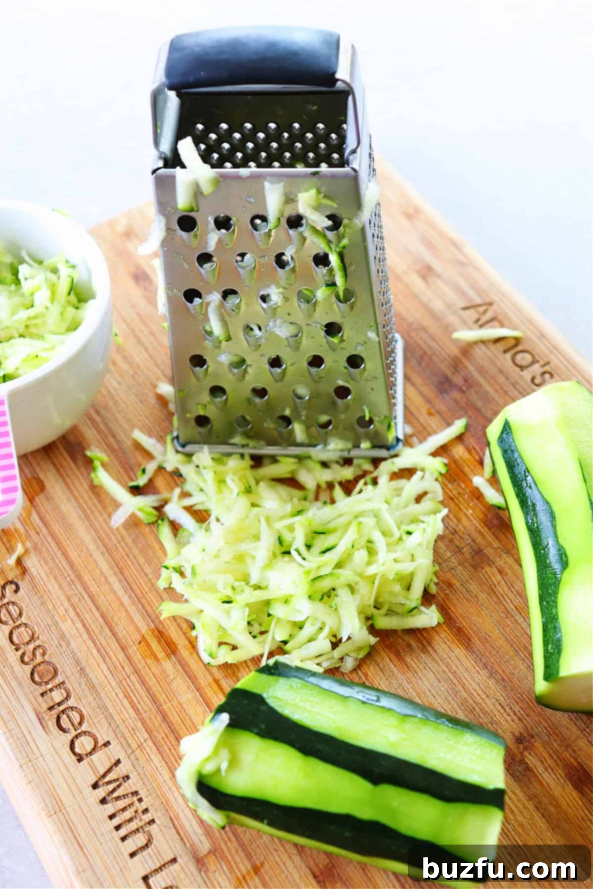 Shredded zucchini and a box grater on a rustic wooden cutting board.