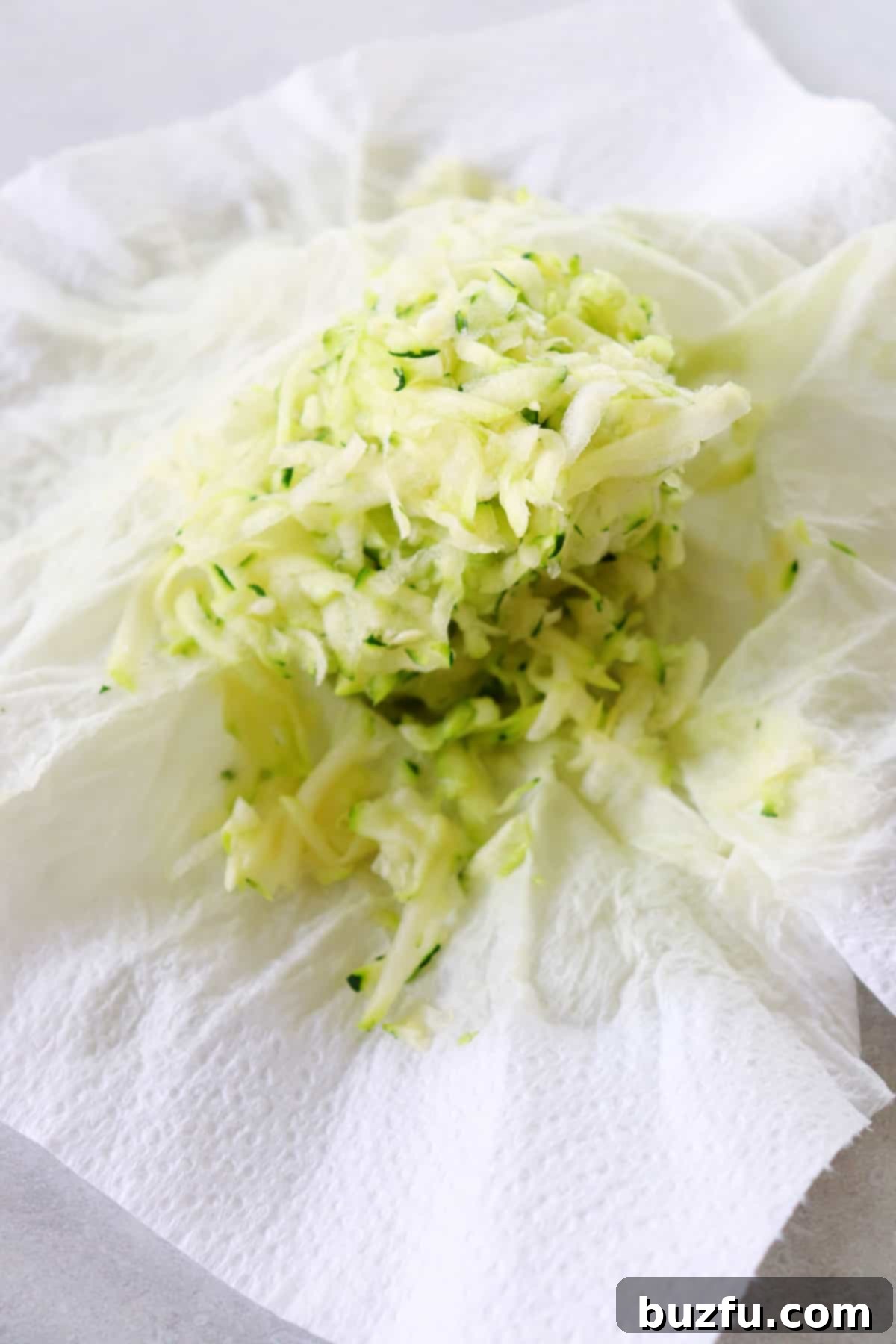Squeezed shredded zucchini on paper towels, demonstrating moisture removal.
