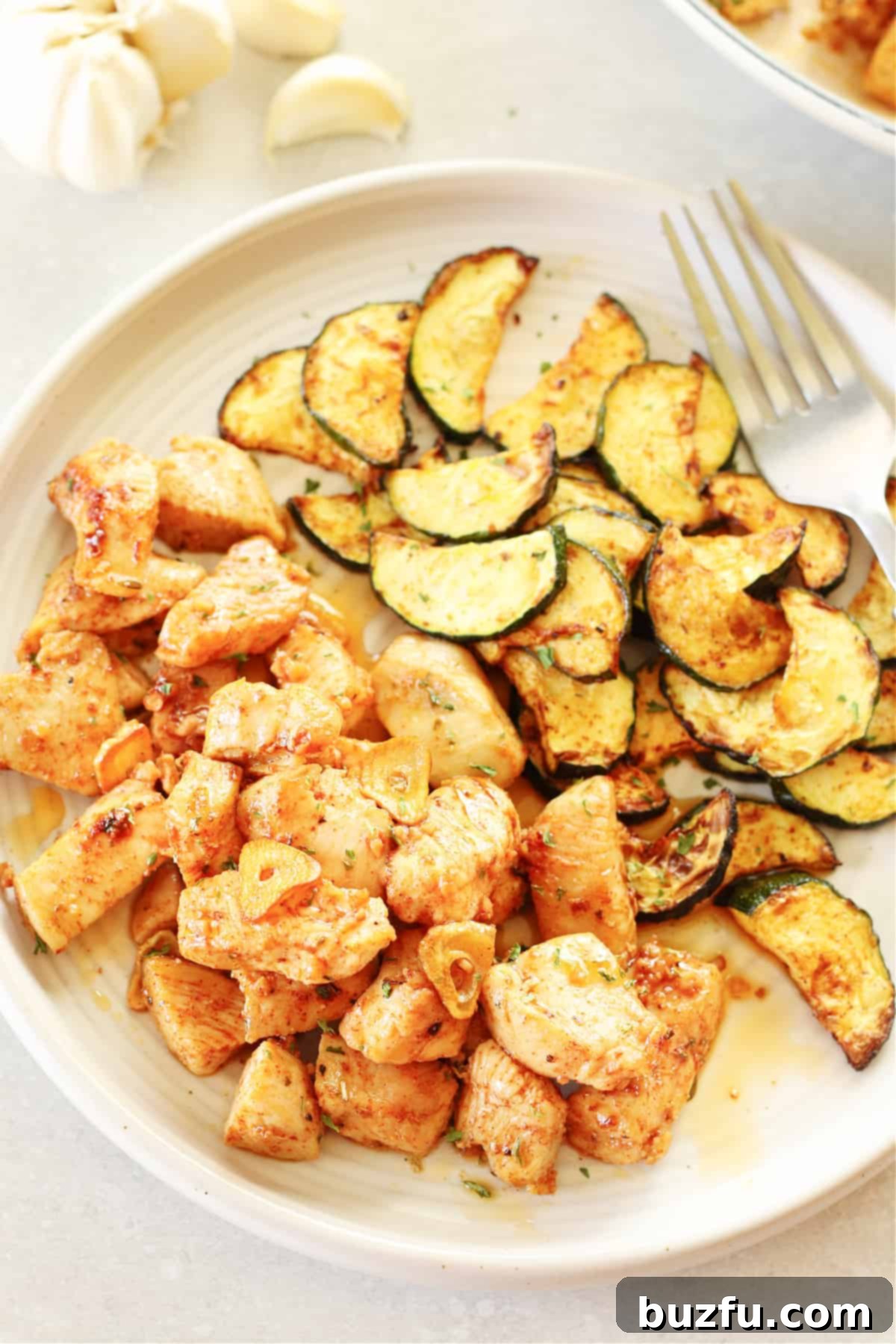 Chicken Bites with Garlic Butter Sauce Plated chicken bites with garlic butter sauce and cooked zucchini slices on a white dinner plate.