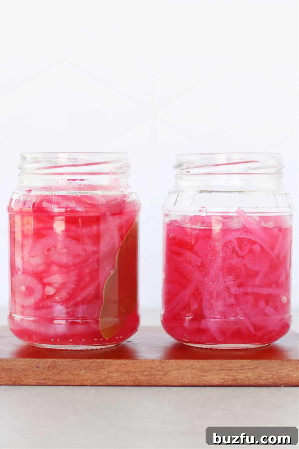 Two jars of freshly made quick pickled red onions on a rustic wooden board, ready to be served or stored.