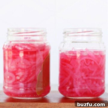 Two jars of pickled red onions on a wooden board.