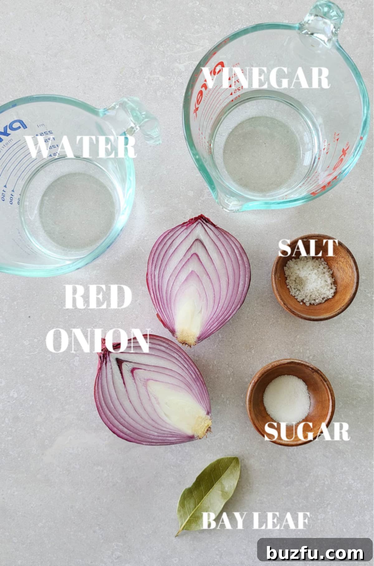 All the necessary ingredients for making pickled red onions laid out on a gray cutting board, including a red onion, white vinegar, water, salt, sugar, and a bay leaf.