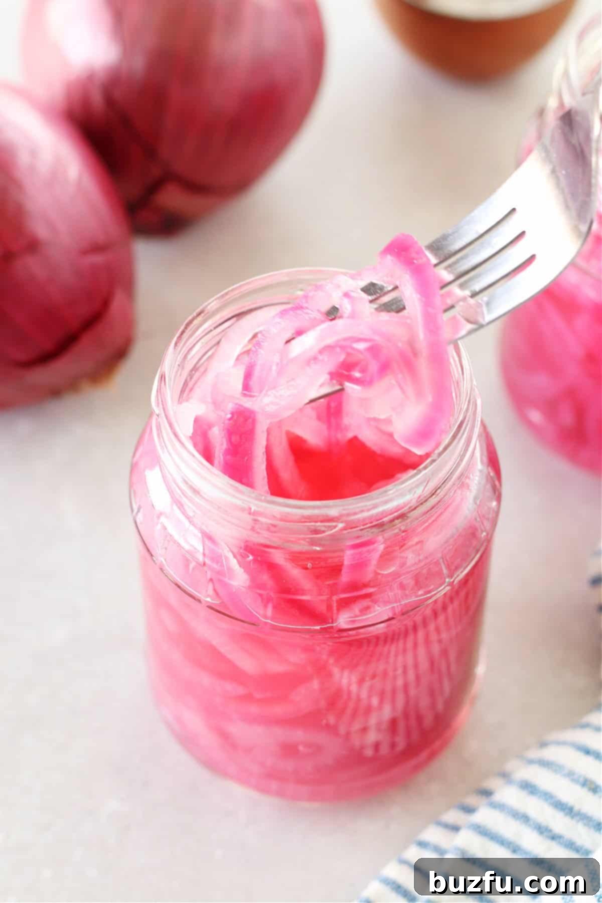A glass jar filled with vibrant pickled red onions, with some onions lifted on a fork, showcasing their appetizing appearance and texture.