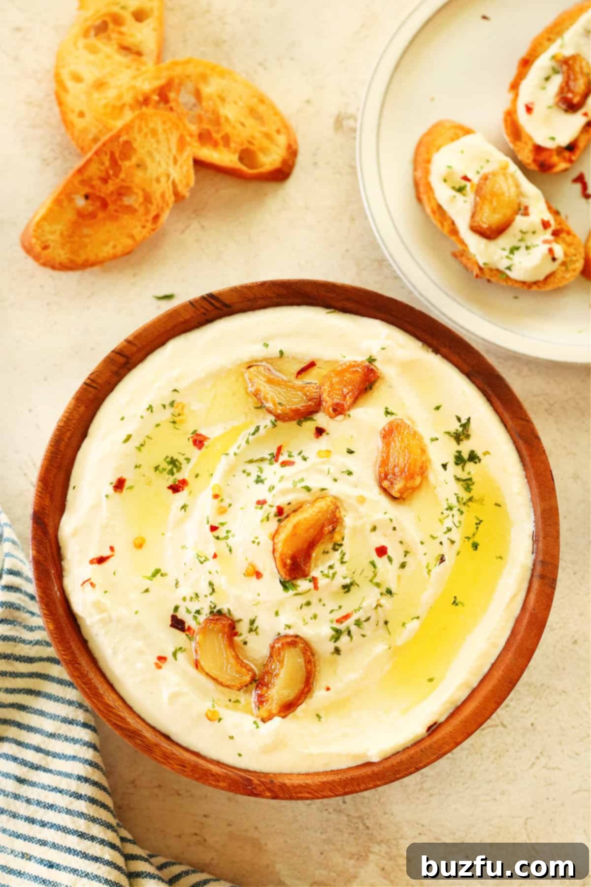 Feta dip with garlic in a wooden bowl on cream board.