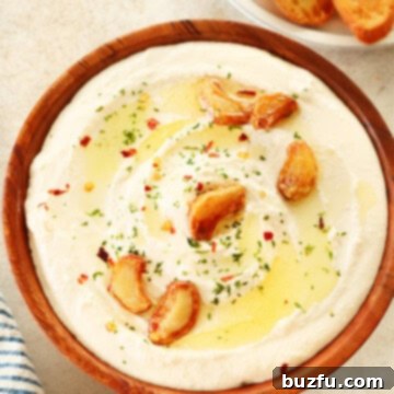 Feta dip with roasted garlic cloves in a wooden bowl on a cream board.