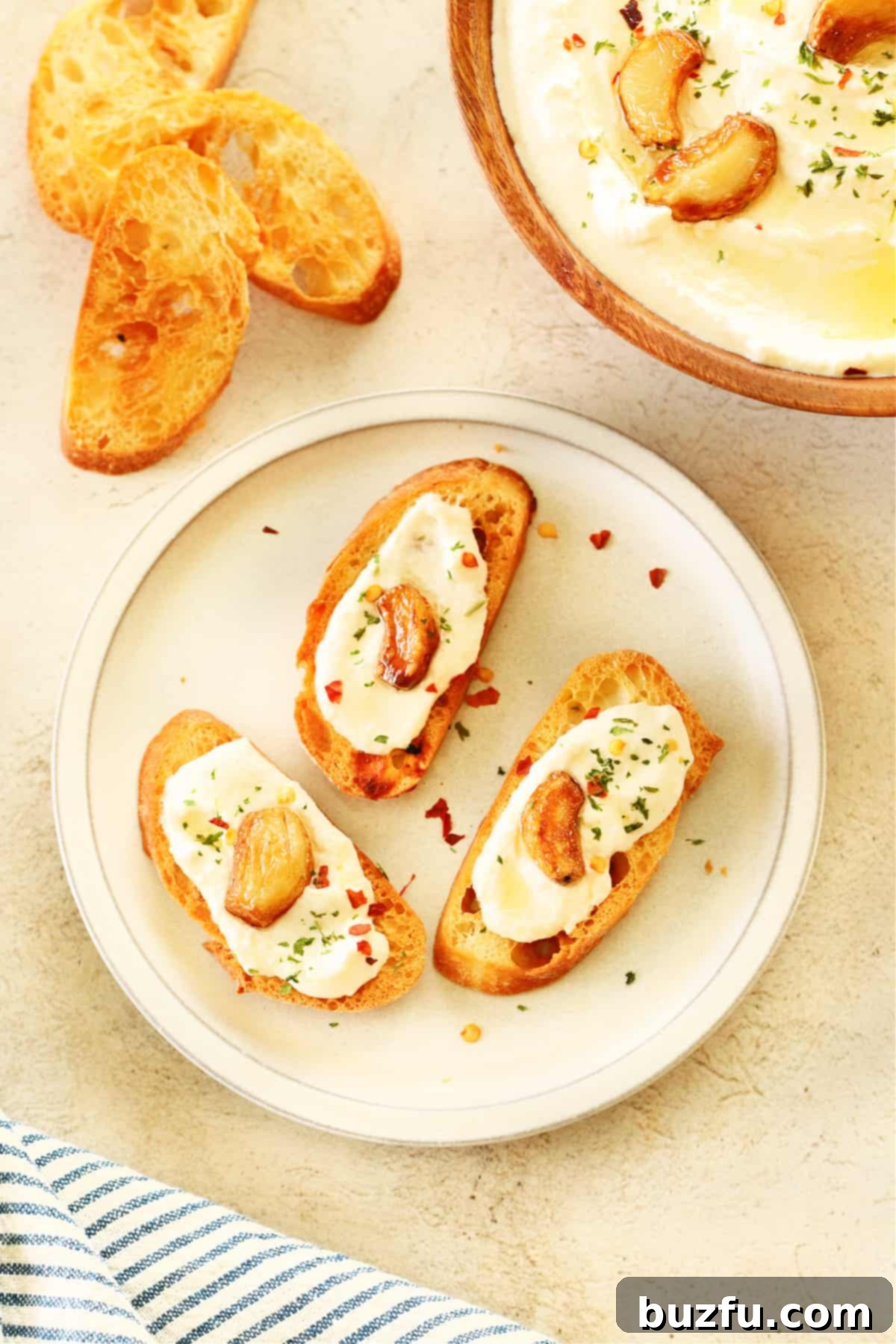 Three slices of baguette with feta dip and roasted garlic on a small plate.
