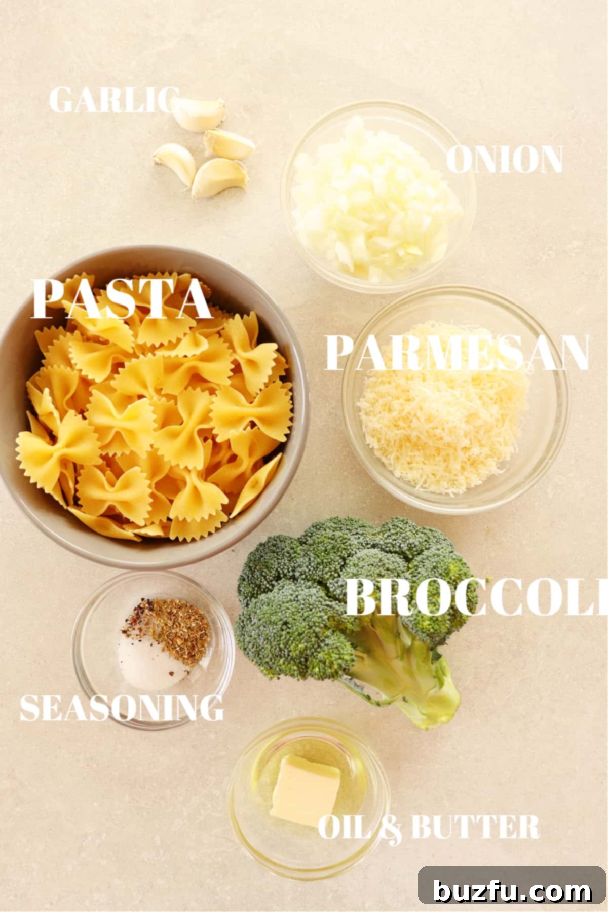 Fresh ingredients for broccoli pasta laid out on a gray cutting board, including pasta, broccoli florets, onion, garlic, olive oil, and butter.