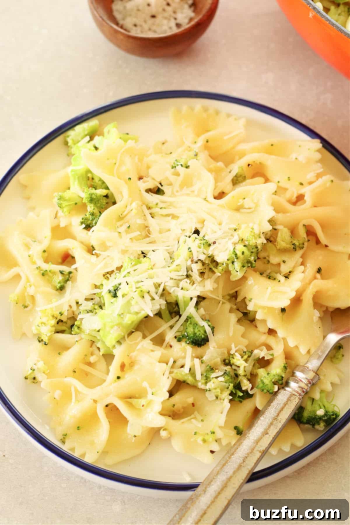 A serving of bow tie pasta and broccoli on a elegant white plate with a blue rim, garnished with fresh parsley.