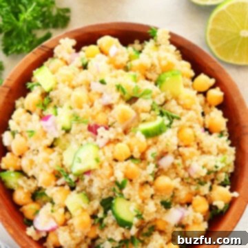 Quinoa salad with chickpeas and cucumber in a wooden bowl on cream background.