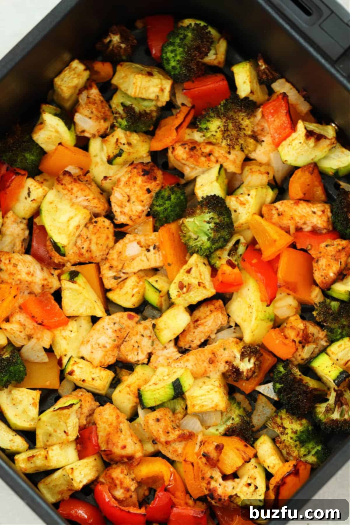 Cooked chicken and veggies in the air fryer basket, showing a golden brown finish and vibrant colors.