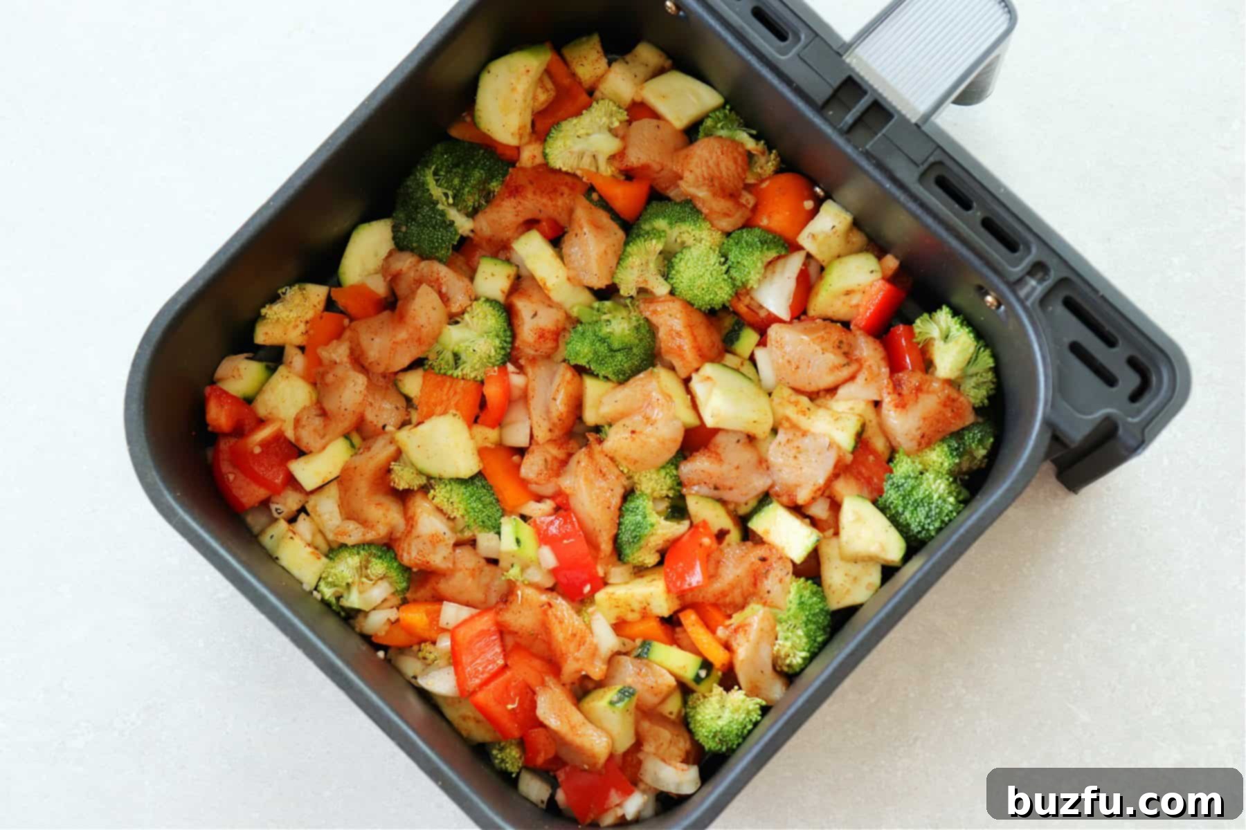 Raw chicken and vegetables arranged in a single layer inside an air fryer basket, ready for cooking.