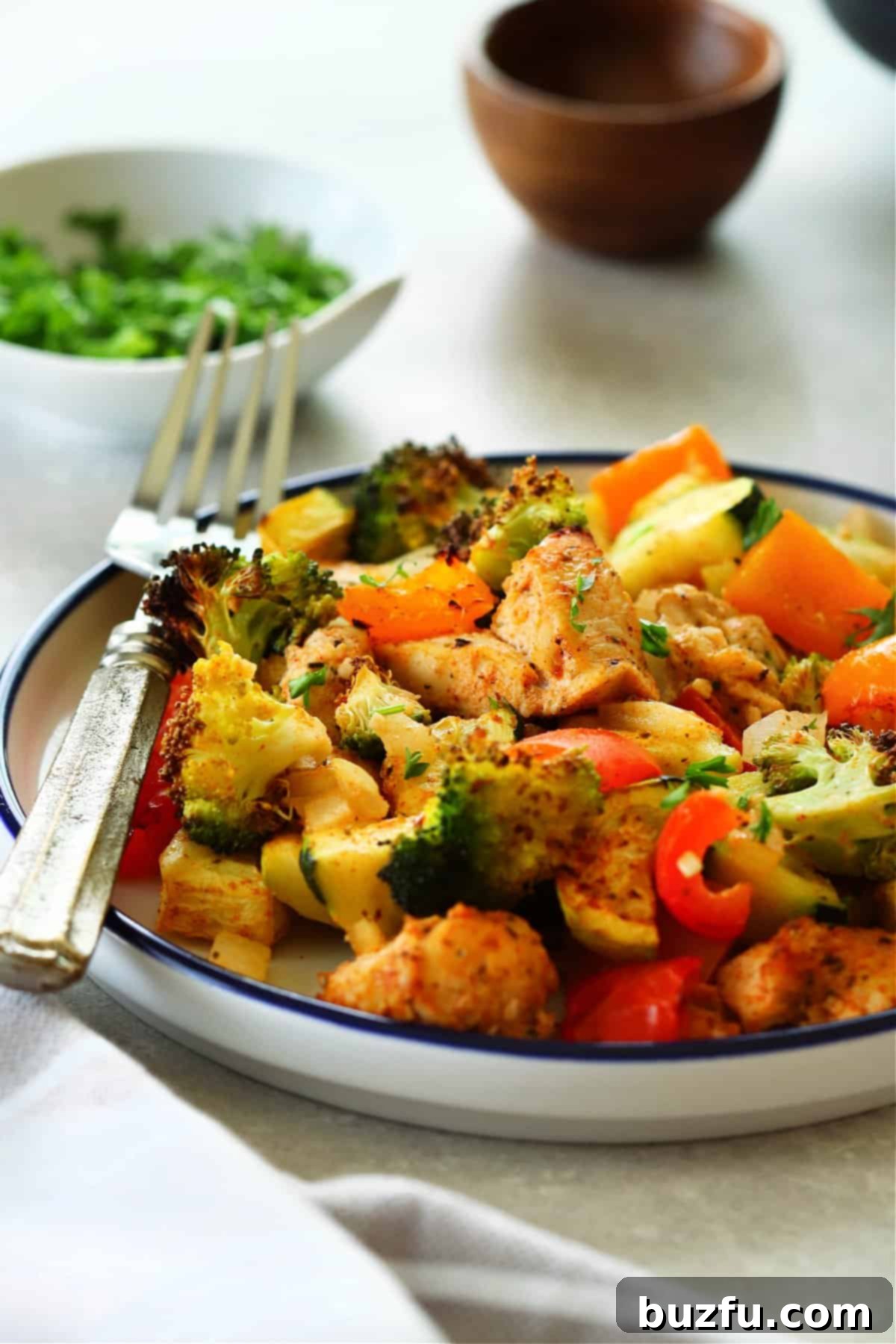 Side shot of perfectly cooked air fryer chicken and vegetables served on a blue-rimmed plate with a fork.
