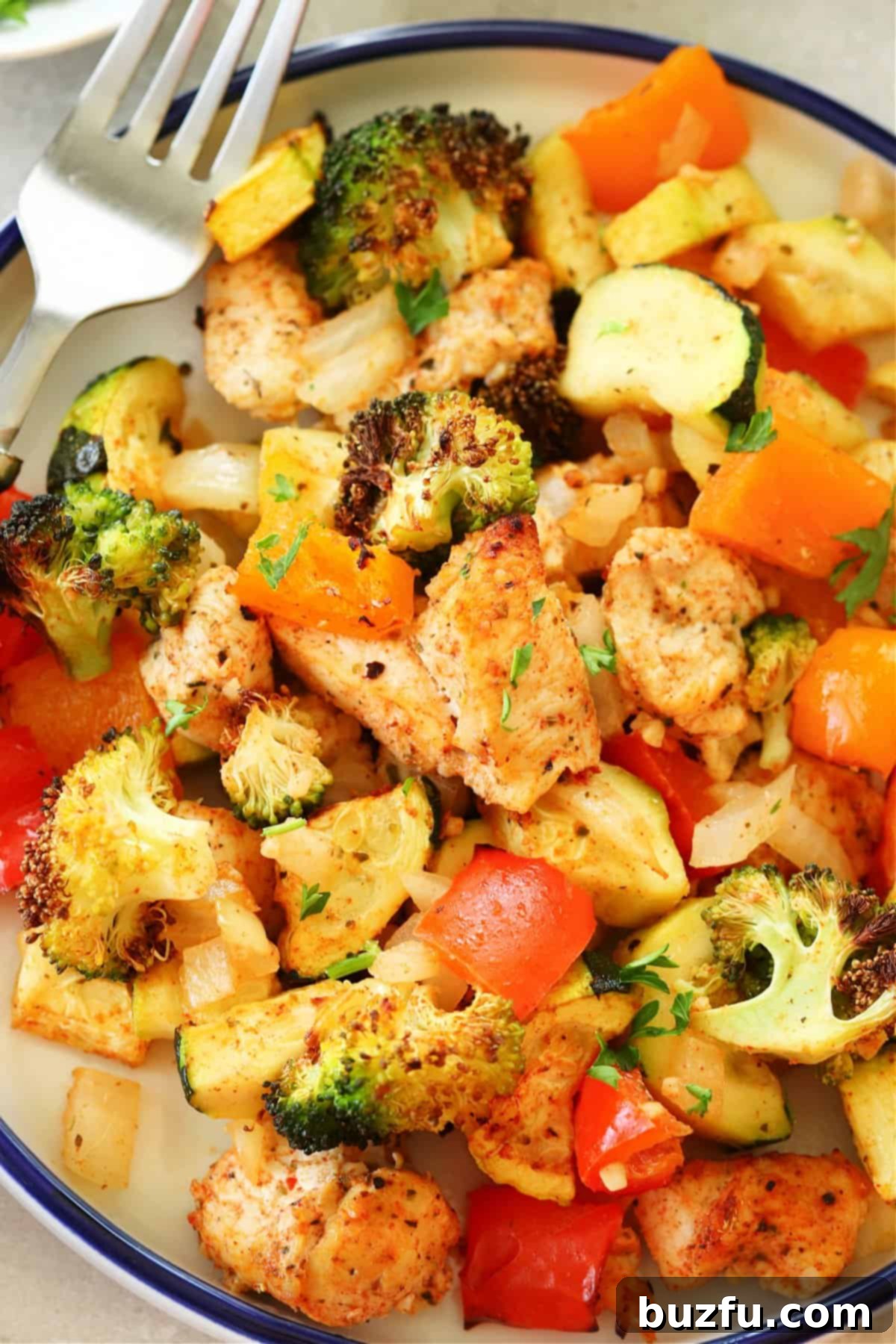 Easy air fryer chicken and vegetables arranged artfully on a white plate with a blue rim, highlighting the fresh garnish.