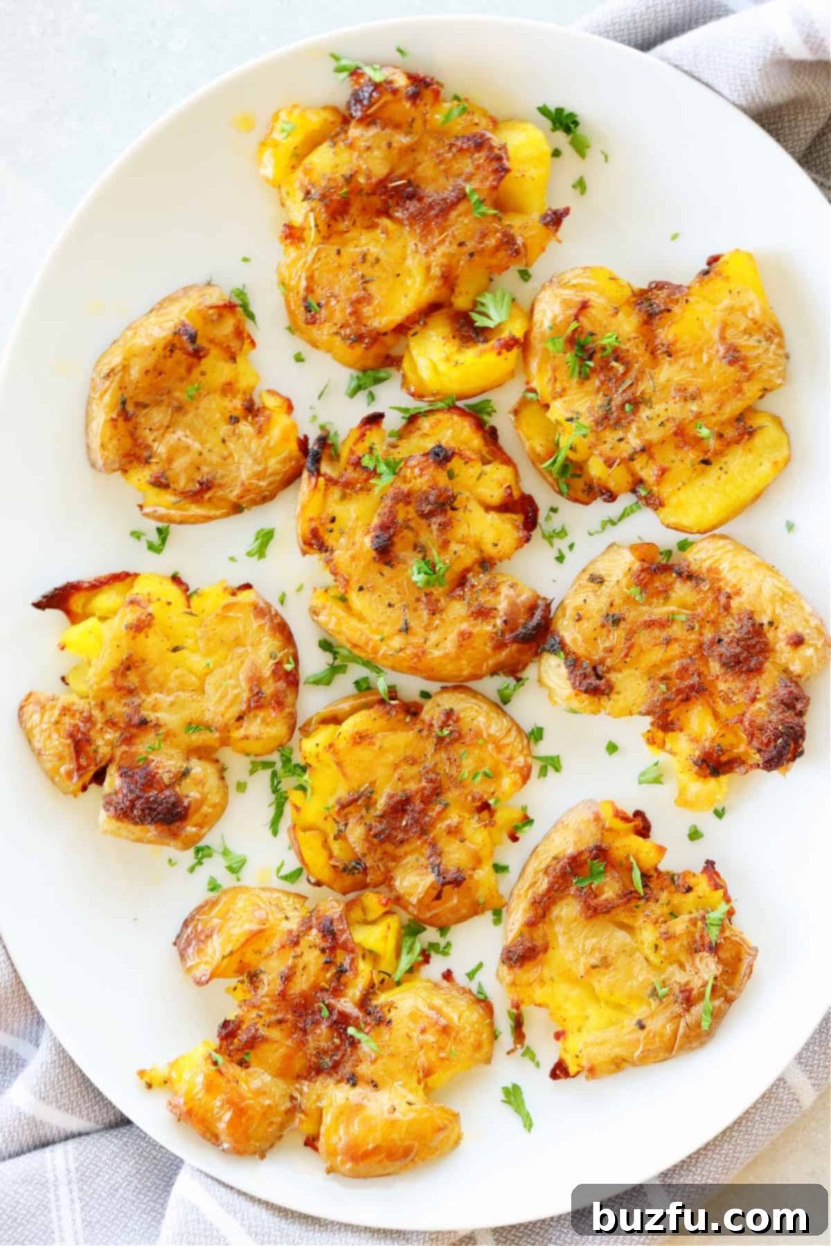 Effortless Crispy Smashed Potatoes 6 Several smashed potatoes on a white serving dish with kitchen towel underneath.