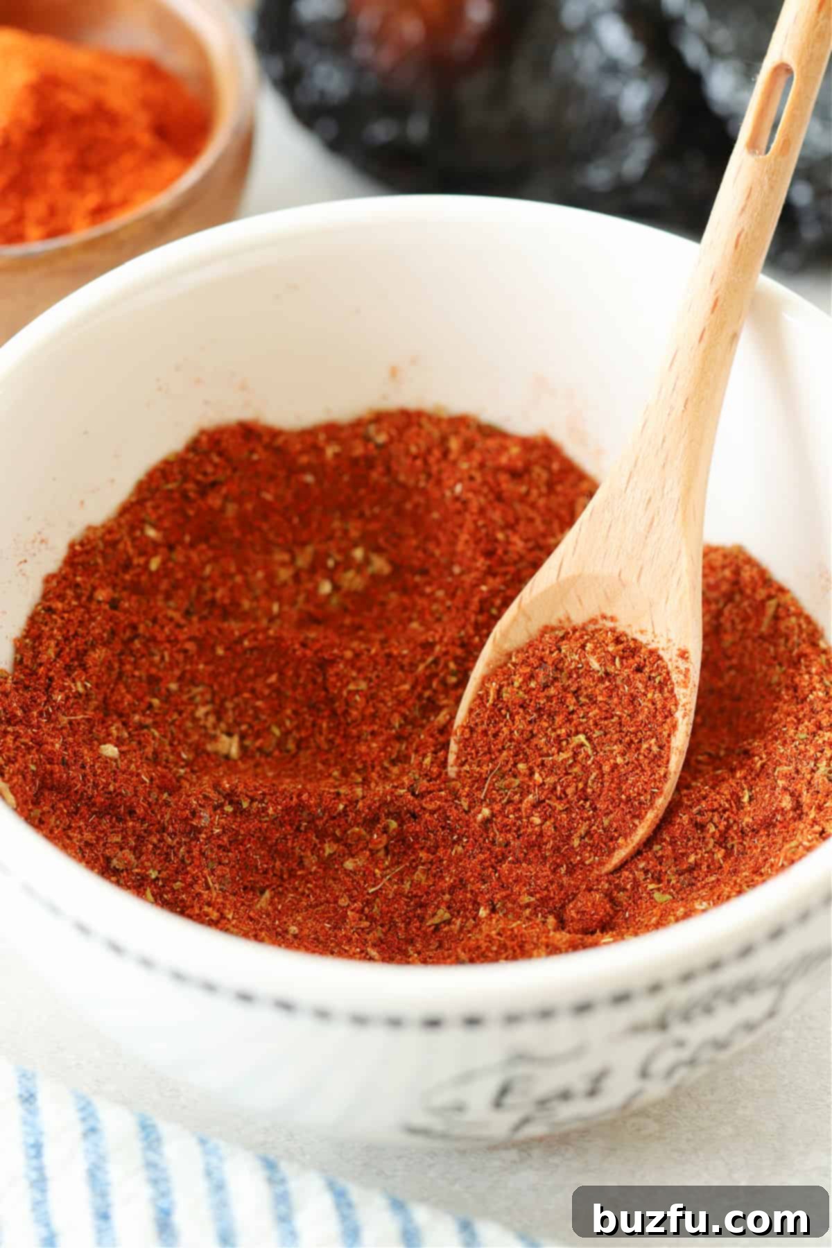 Craft Your Perfect Chili Blend 4 Chili seasoning in a white bowl with a small wooden spoon.