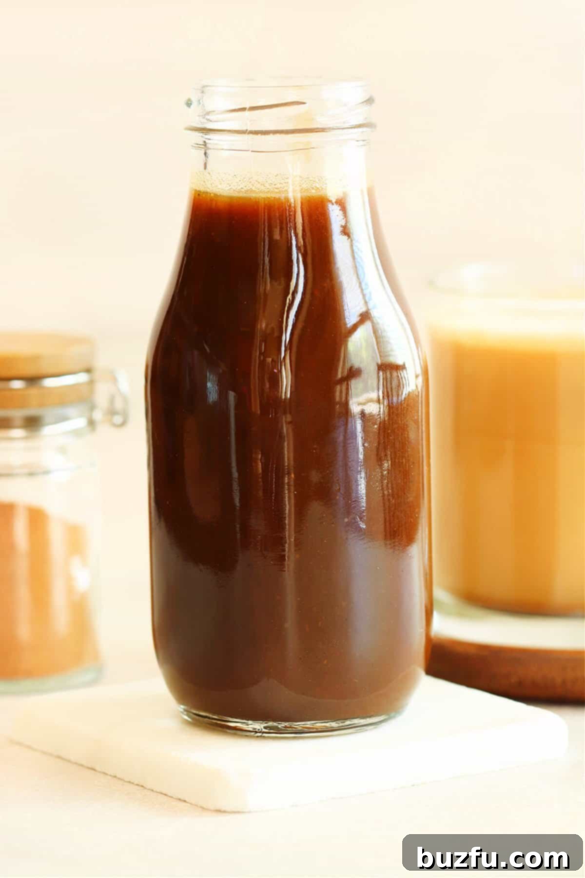 Pumpkin syrup in a glass bottle on a marble coaster, ready for use in fall beverages and desserts.