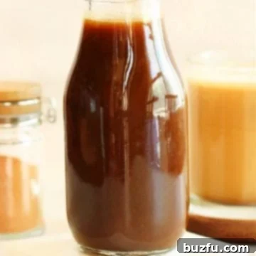 Pumpkin syrup in a glass bottle on a marble coaster.