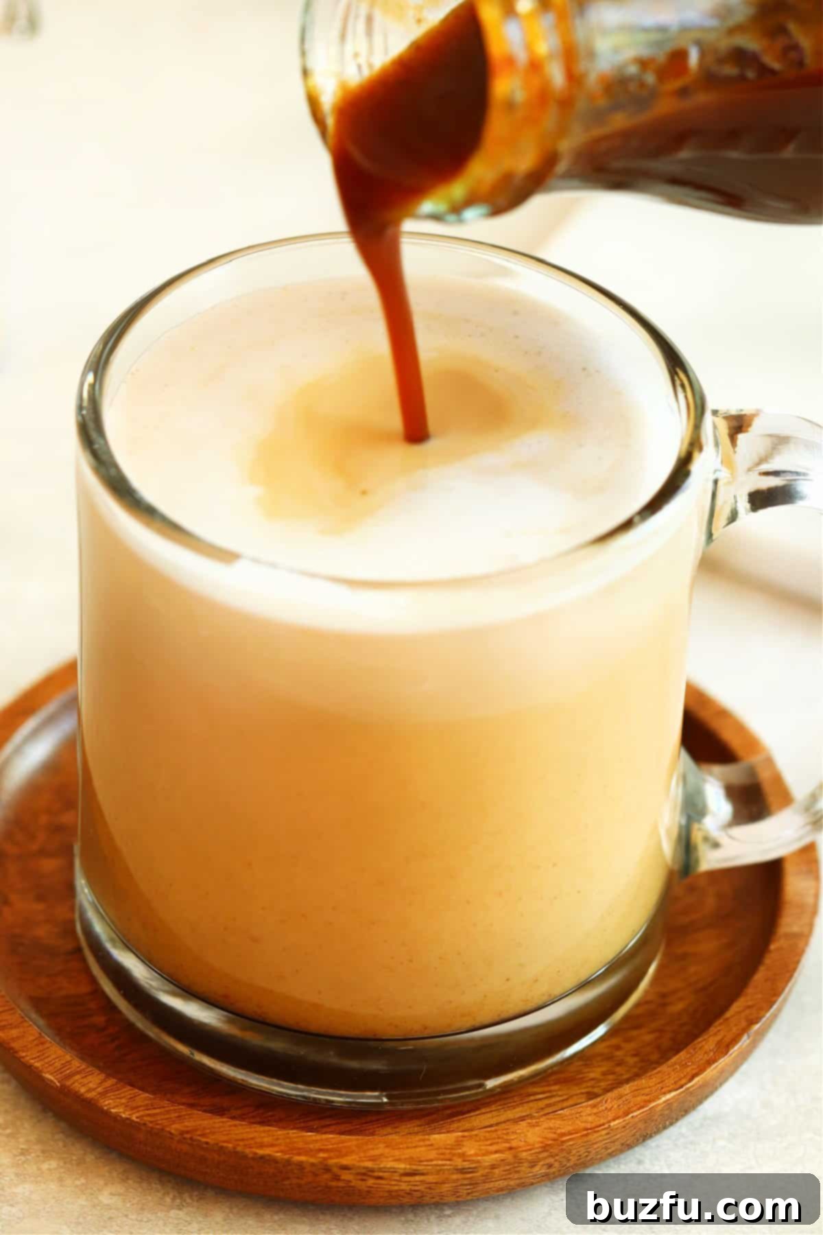 Pumpkin syrup being poured into a glass mug of coffee, creating a swirling pattern.