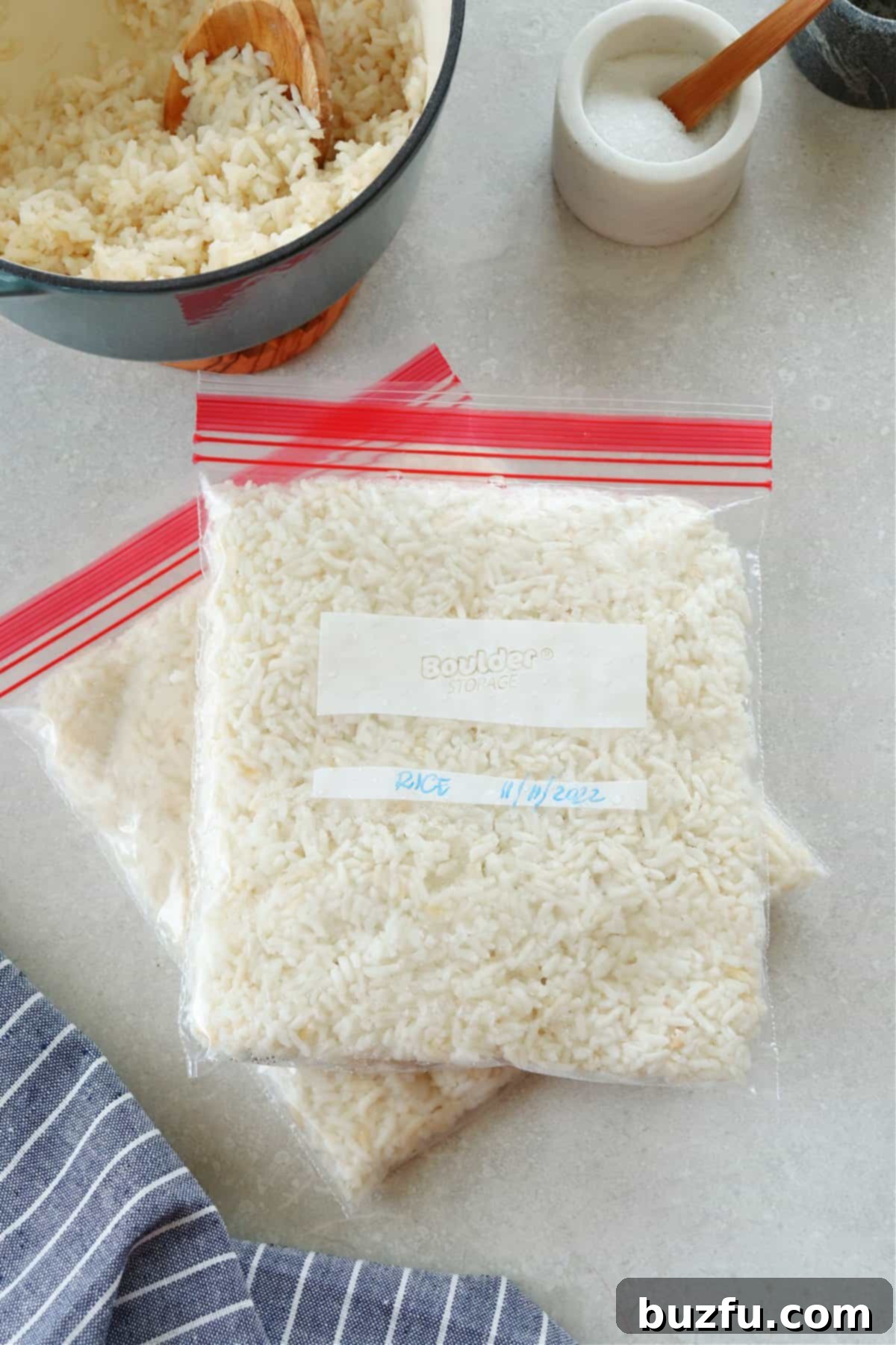 Unlock the Secret to Perfectly Frozen Rice 2 Freshly cooked rice meticulously portioned into transparent freezer bags, neatly arranged on a gray cutting board. A wooden bowl of uncooked rice kernels sits nearby, emphasizing the journey from grain to freezer-ready convenience.