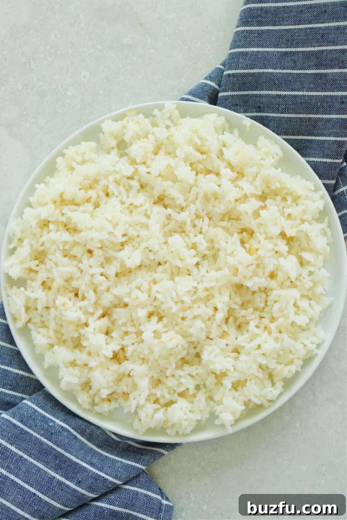 Unlock the Secret to Perfectly Frozen Rice 3 Close-up view of freshly cooked, fluffy white rice spread evenly on a white ceramic plate, cooling down to prepare for the freezing process.
