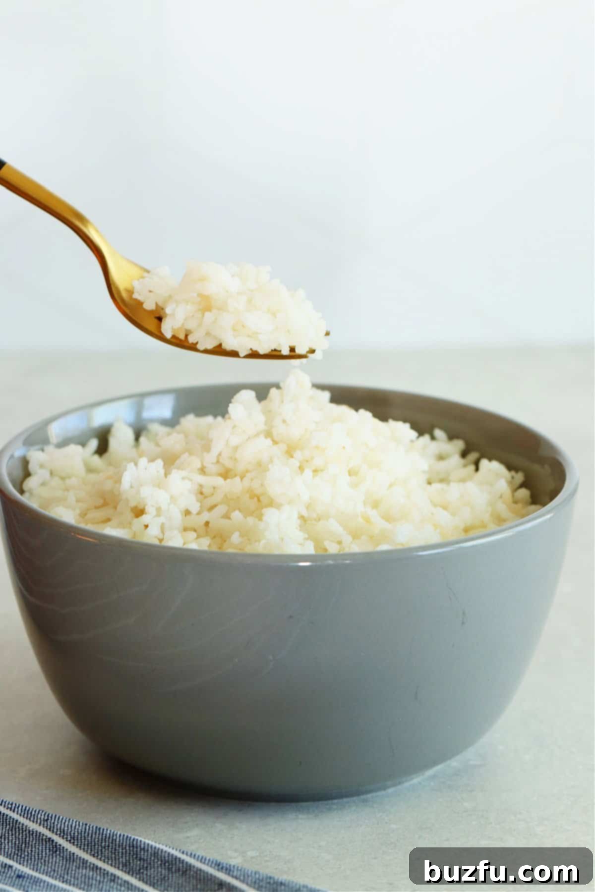 Unlock the Secret to Perfectly Frozen Rice 4 A elegant gray bowl brimming with fluffy, reheated white rice, with a fork poised above, holding a spoonful of rice, ready to be enjoyed.