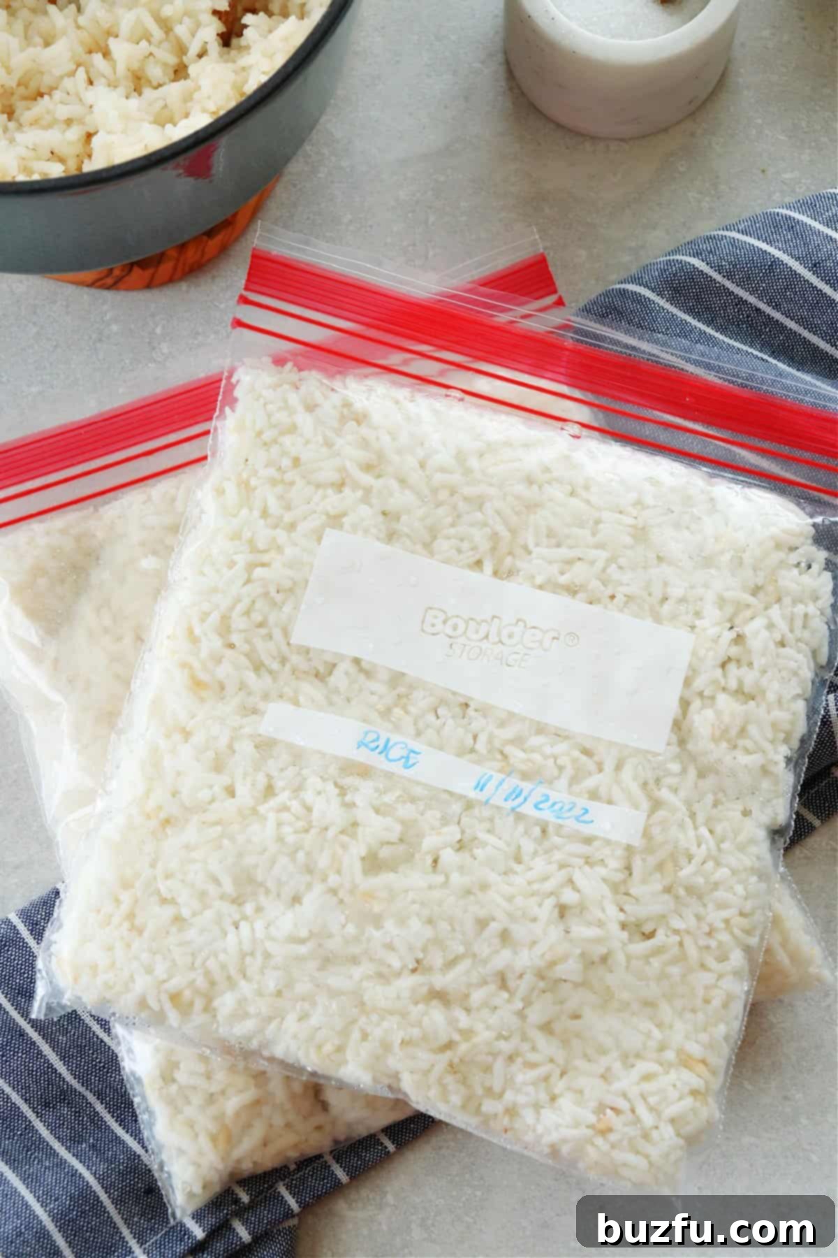 Unlock the Secret to Perfectly Frozen Rice 5 Two transparent freezer bags filled with perfectly portioned, cooked white rice, flattened and ready for efficient freezer storage, resting on a rustic gray board.
