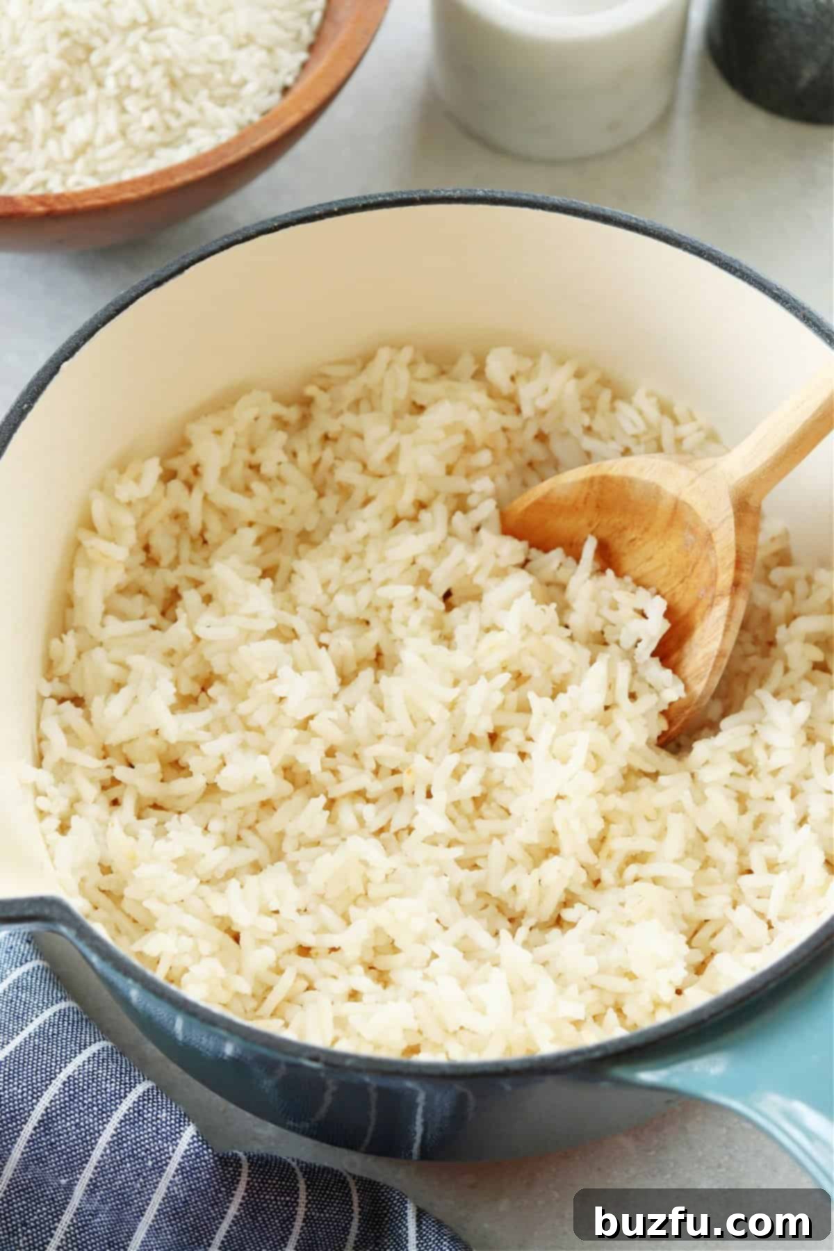 Perfectly cooked white rice, fluffed and ready to serve, in a saucepan with a wooden spoon.