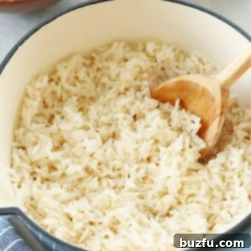 Cooked white rice in a saucepan with a wooden spoon inside, illustrating the perfect texture.