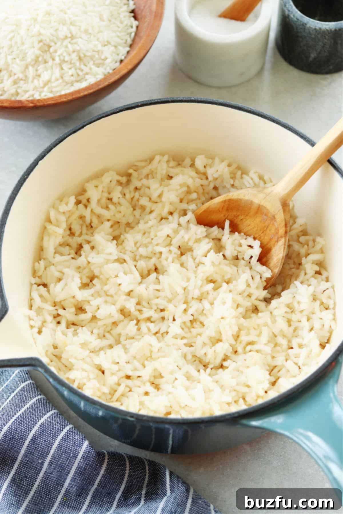 Cooked rice in a blue pot with a wooden spoon inside and a blue napkin on the side, ready to be served.