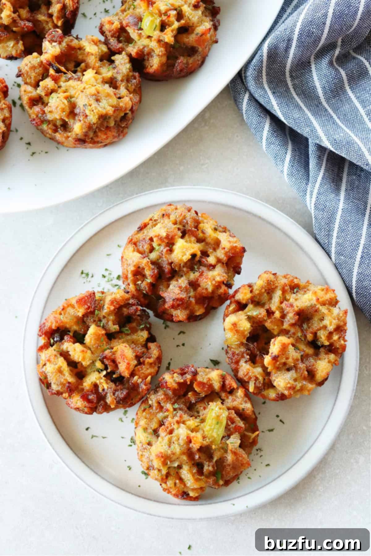 Savory Stuffing Cupcakes 2 Four golden-brown stuffing muffins artfully arranged on a white plate, with a rustic kitchen towel nearby, highlighting their crispy tops and inviting texture.