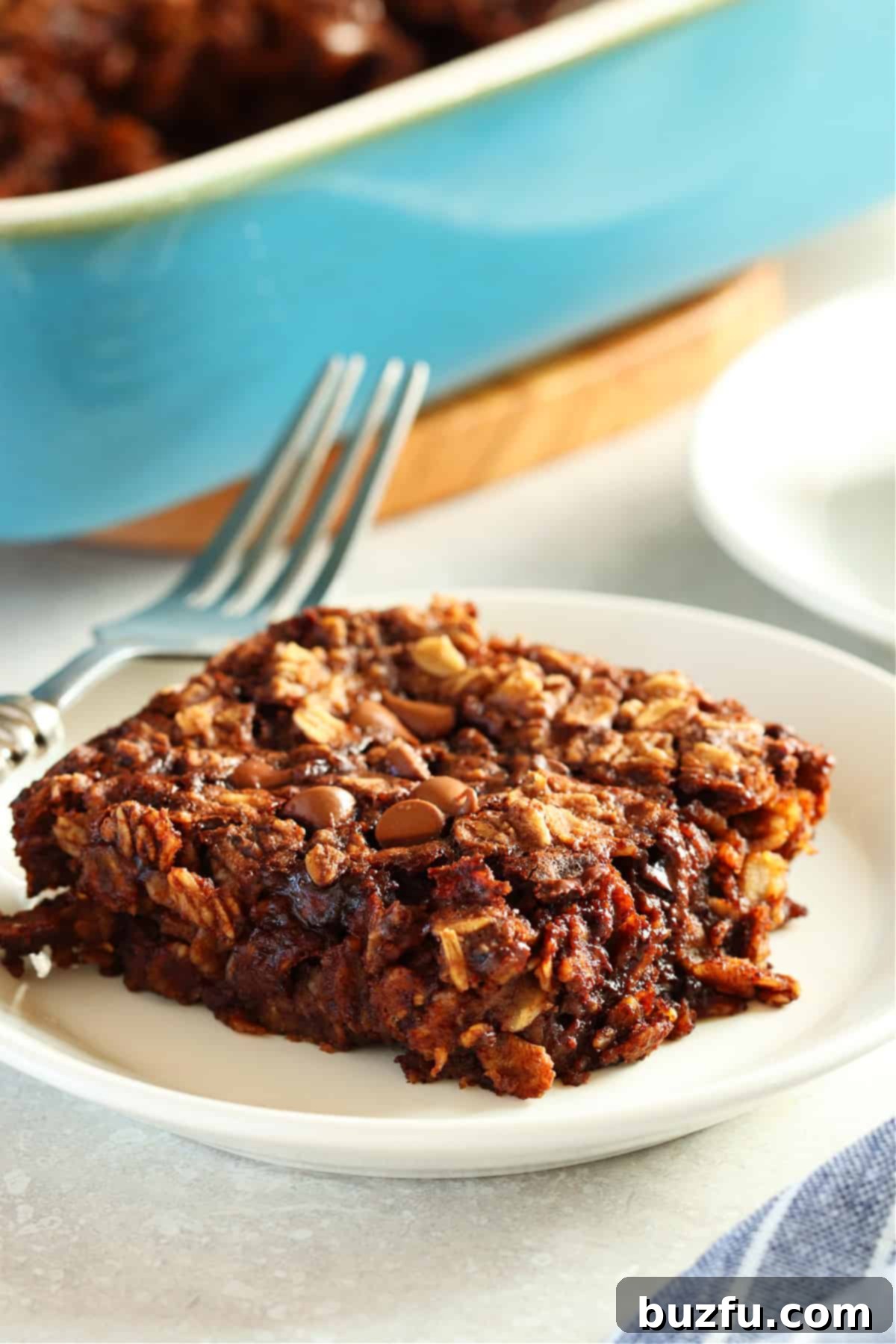 One serving of healthy baked chocolate oatmeal on a small white plate with the baking dish in the background, ready for breakfast.
