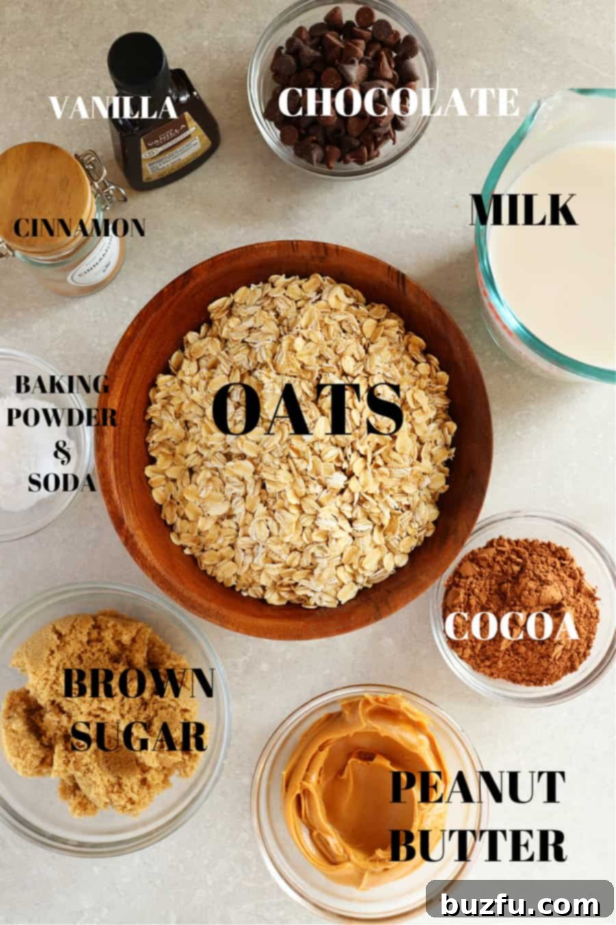 Oats, brown sugar, peanut butter, cocoa powder, milk, cinnamon, vanilla, baking powder and soda in glass containers on a gray board for baked chocolate oatmeal.