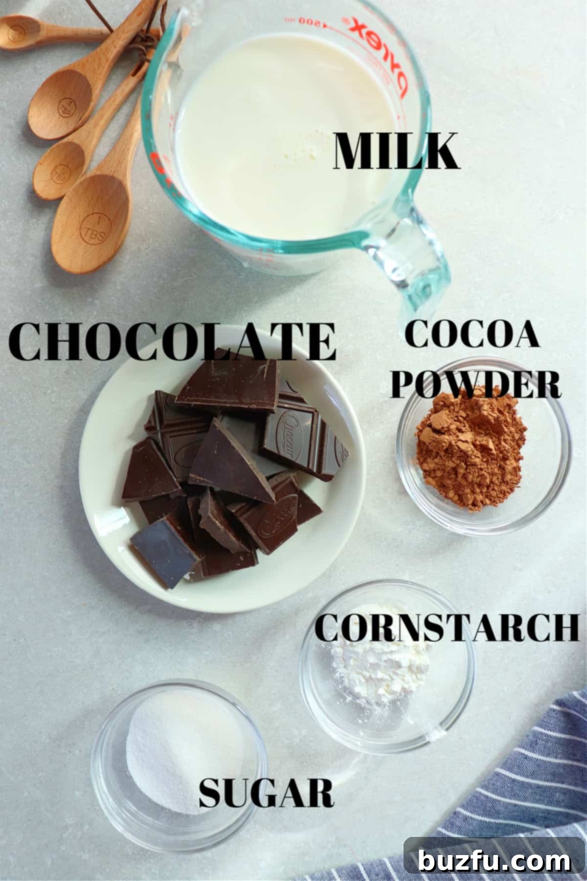 Chocolate, cocoa powder, sugar, cornstarch and milk in glass bowls on a gray background.