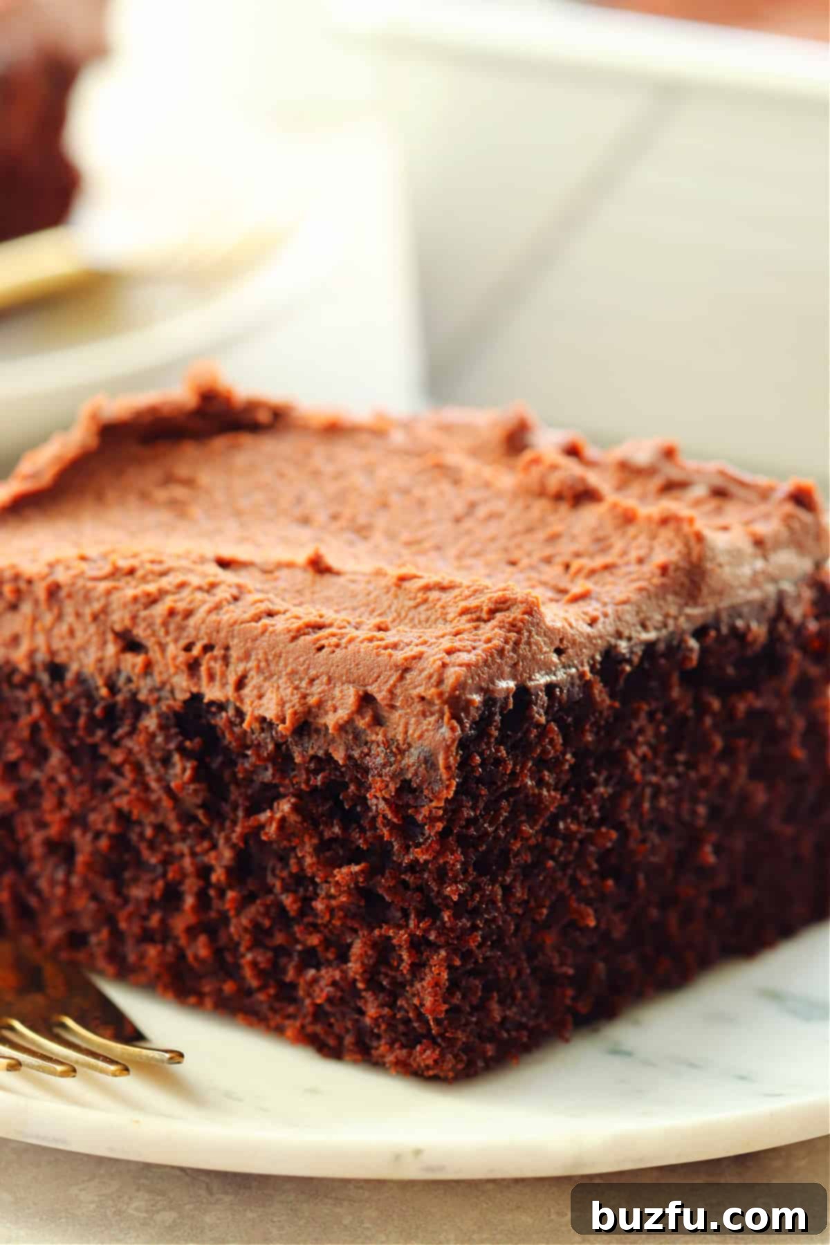 Decadent Eggless Chocolate Delight 2 A piece of chocolate cake with chocolate frosting on a marble plate with gold fork.