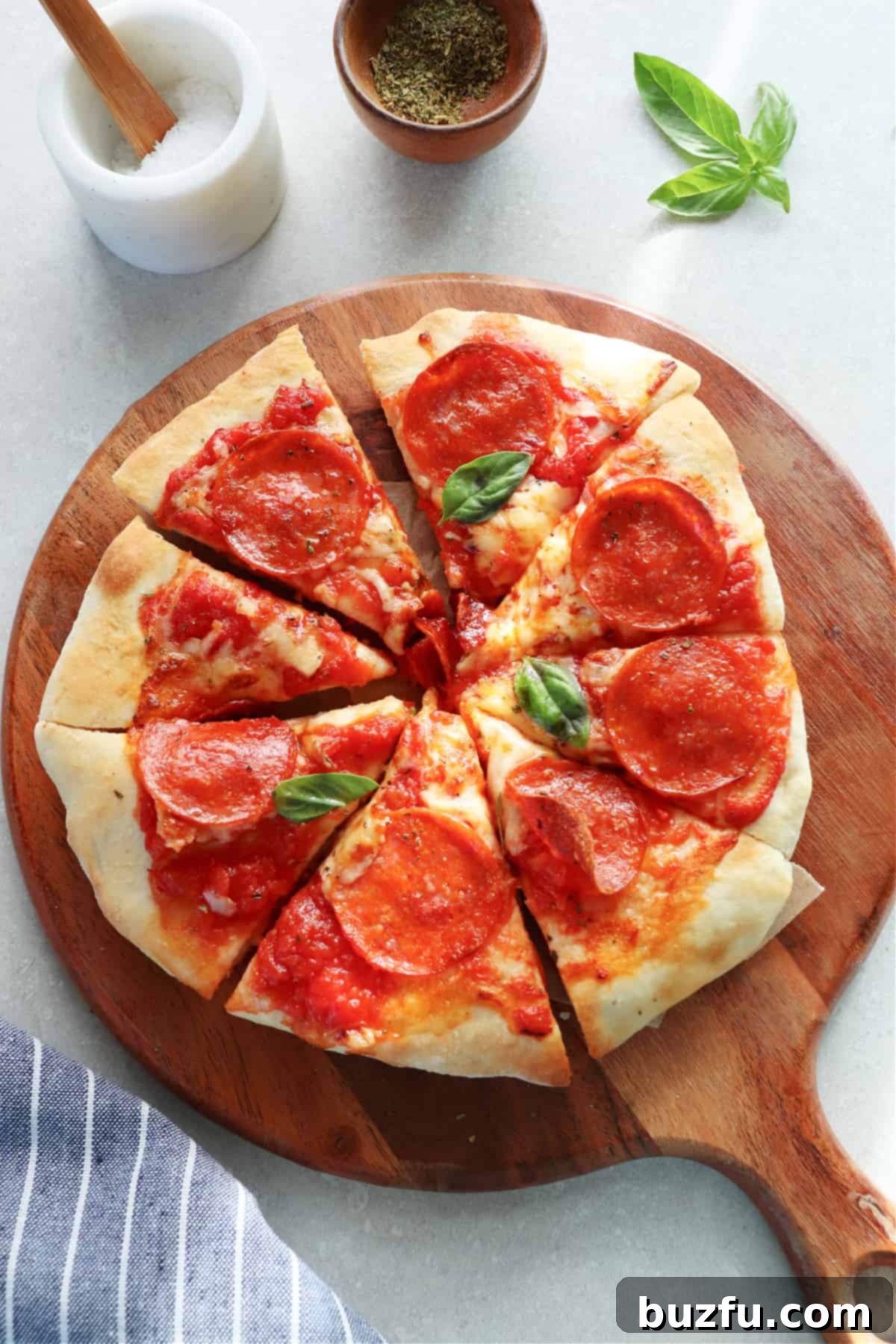 Freshly sliced air fryer pizza on a wooden board, garnished with basil leaves, and accompanied by small cups of salt and seasoning.