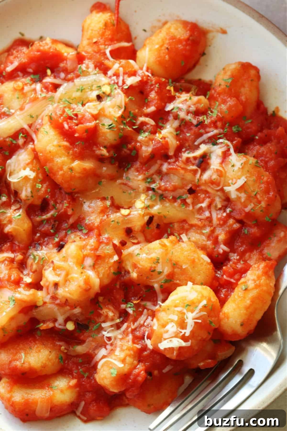 Gnocchi in tomato sauce with Parmesan on a cream plate.