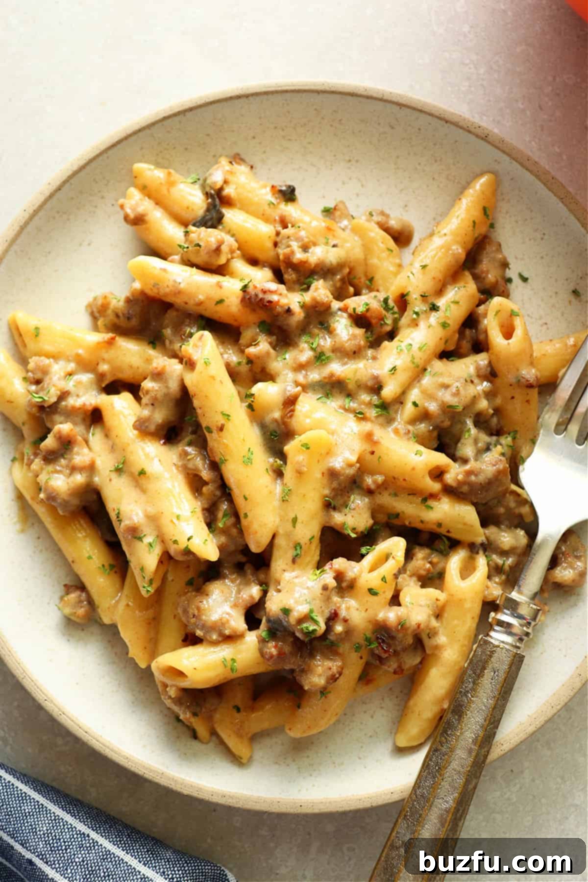 Penne with sausage and creamy sauce on a gray plate with fork.