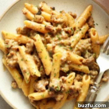 Penne with sausage and creamy sauce on a gray plate with fork.