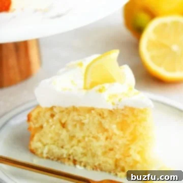 One slice of lemon cake with whipped cream and a small slice of lemon on a dessert plate with gold fork.