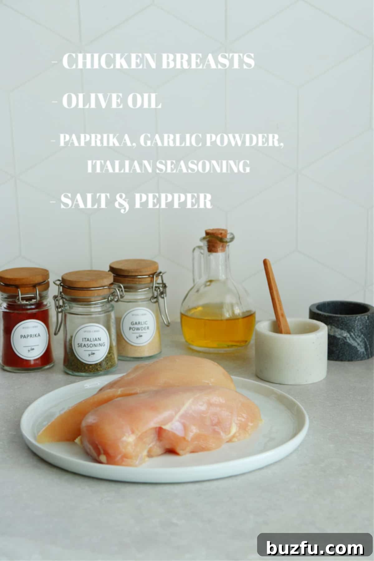 Jars with spices, raw chicken breast on a plate, salt and pepper in bowls and oil in a cruet on a kitchen counter.