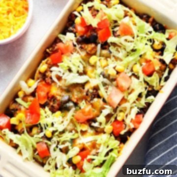 A baked casserole with taco meat, fresh tomatoes, and lettuce, served in a rectangular baking dish.