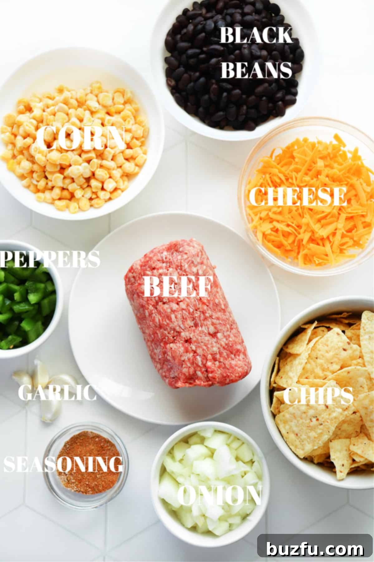 All fresh ingredients for a homemade taco casserole laid out on a white tiled surface.