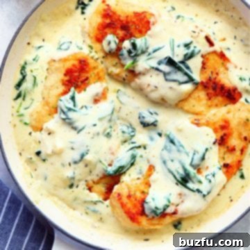 Three chicken breasts in a creamy sauce with spinach, in an enameled Le Creuset skillet.