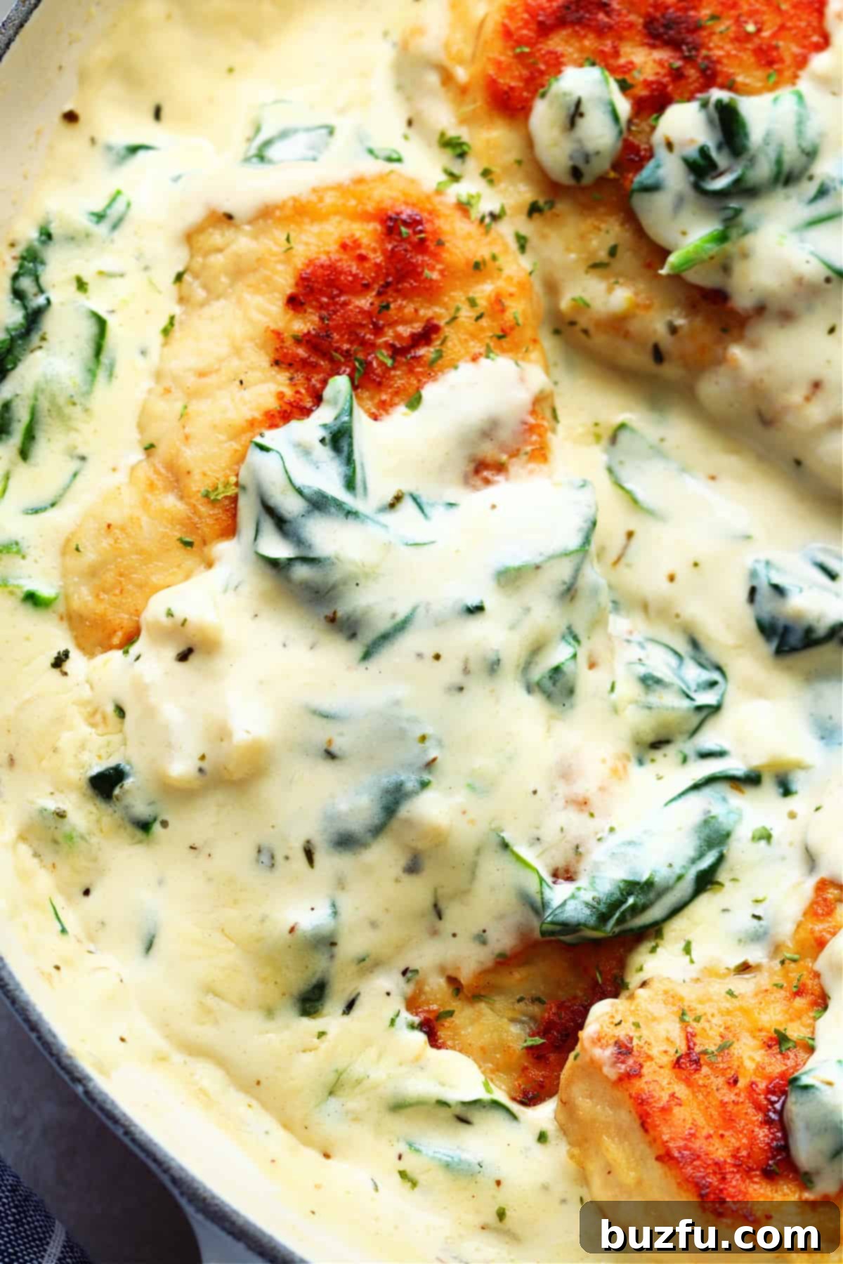 A succulent cooked chicken breast glistening in a creamy sauce with vibrant spinach, artfully presented in a pan.